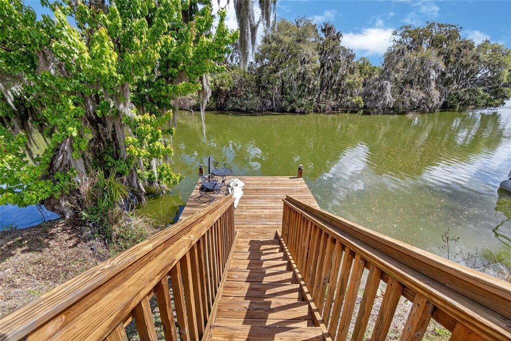 A wooden staircase leads down to a small dock overlooking a calm, tree-lined lake — 6870 SHIMMERING DRIVE, LAKELAND, FL