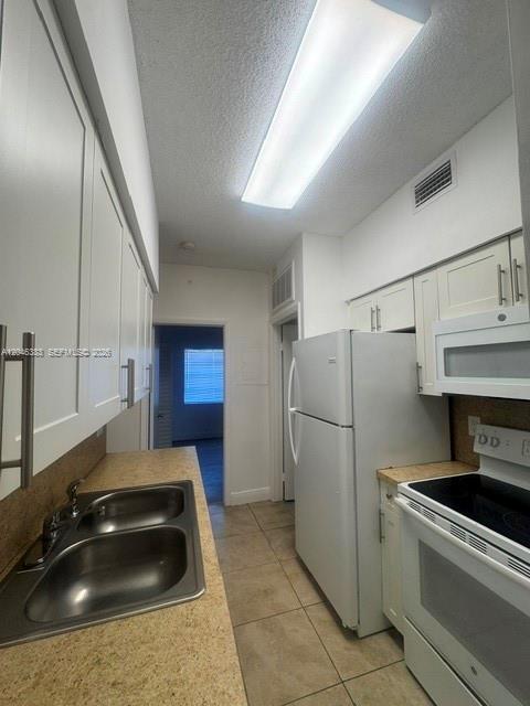 A galley kitchen features white cabinets, a double sink, and white appliances on tiled floors — 18336 NW 68th Ave # C, Hialeah FL 33015, HIALEAH, FL