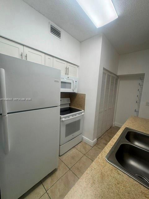 A kitchen with white appliances, light-colored cabinets, a double sink, and beige tile flooring — 18336 NW 68th Ave # C, Hialeah FL 33015, HIALEAH, FL