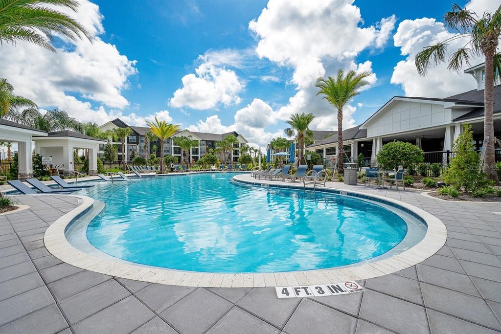 A swimming pool with lounge chairs and palm trees sits in front of apartment buildings — 3020 BASE BOULEVARD UNIT C1, DAVENPORT, FL