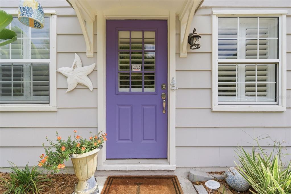 A purple front door with a window sits between two windows on a light-colored house — 652 LEXINGTON STREET, DUNEDIN, FL