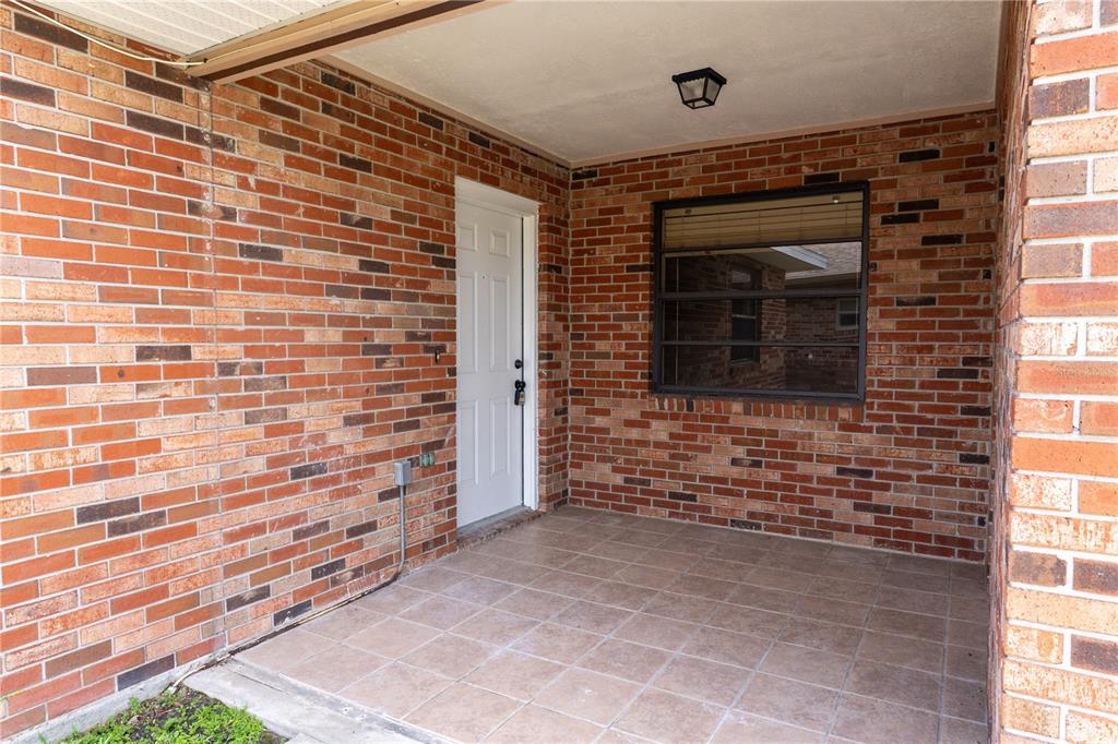 A covered brick porch features a white door, a window, and tiled flooring — 661 LAKE CAROLYN CIRCLE, LAKELAND, FL