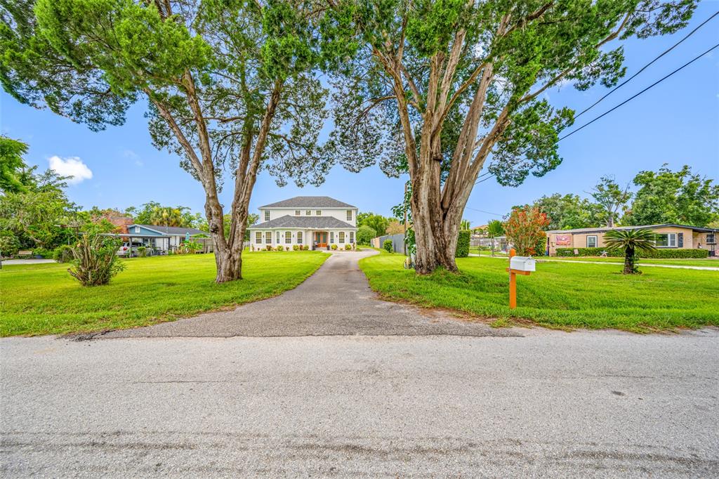 A two-story house with a paved driveway sits behind two large trees on a lawn — 13030 DELWOOD ROAD, TAMPA, FL