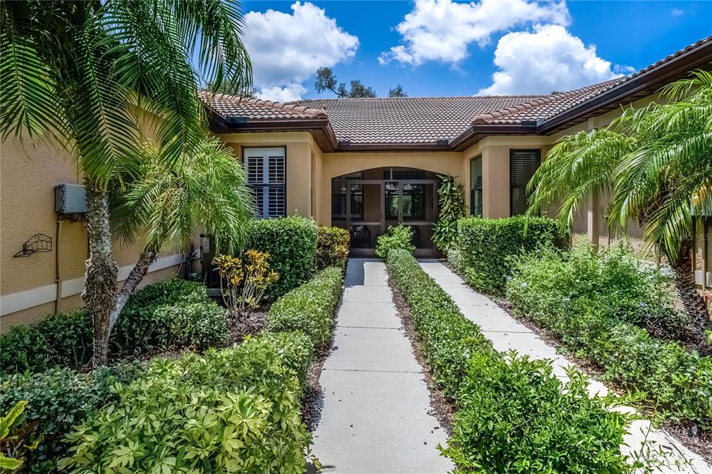 A concrete walkway leads to the screened entryway of a tan house with palm trees — 312 SENECA FALLS DRIVE, APOLLO BEACH, FL