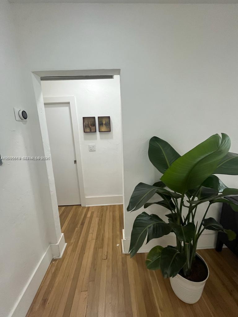 A hallway with light wood flooring leads to a closed white door — 1091 NW 59th St, Miami FL 33127, MIAMI, FL