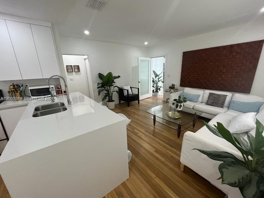 A modern open-concept kitchen and living area features white cabinetry, a central island, and wood flooring — 1091 NW 59th St, Miami FL 33127, MIAMI, FL
