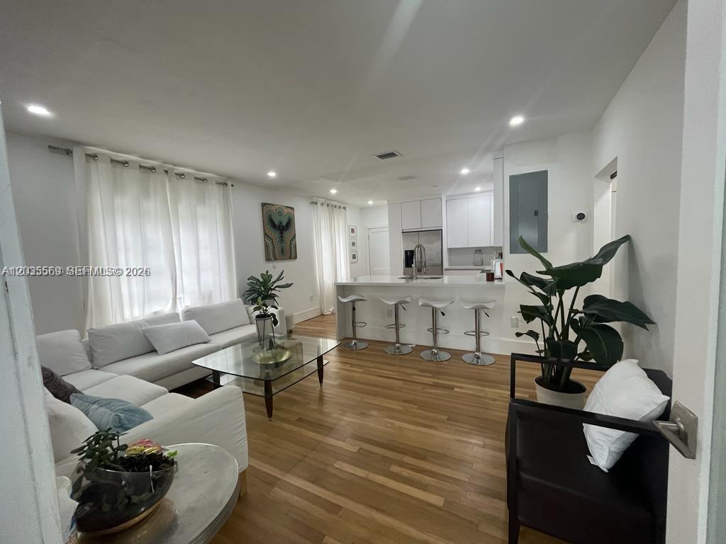 This open-concept living room features white sofas, a glass coffee table, and a kitchen island — 1091 NW 59th St, Miami FL 33127, MIAMI, FL