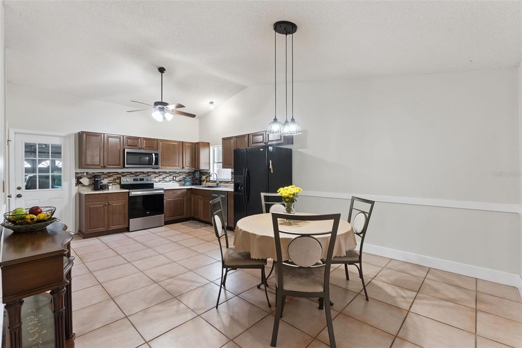 A kitchen with brown cabinets, stainless steel appliances, tile floors, and a round dining table — 15901 SAUSALITO CIR, CLERMONT, FL