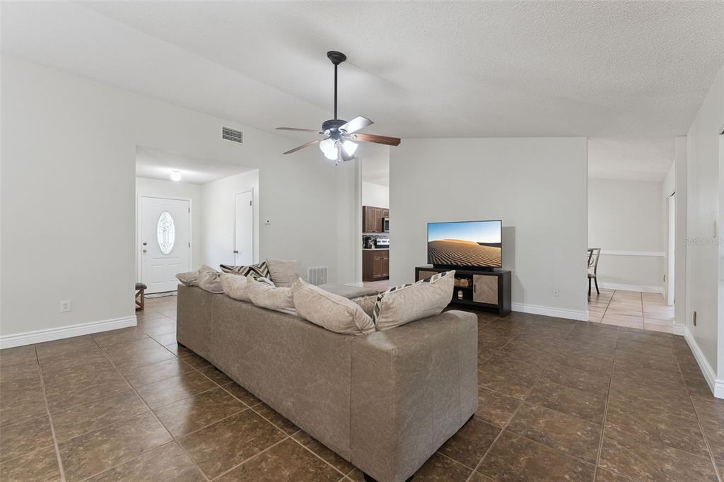 A living room with brown tile floors, a gray sofa, and a television on a stand — 15901 SAUSALITO CIR, CLERMONT, FL