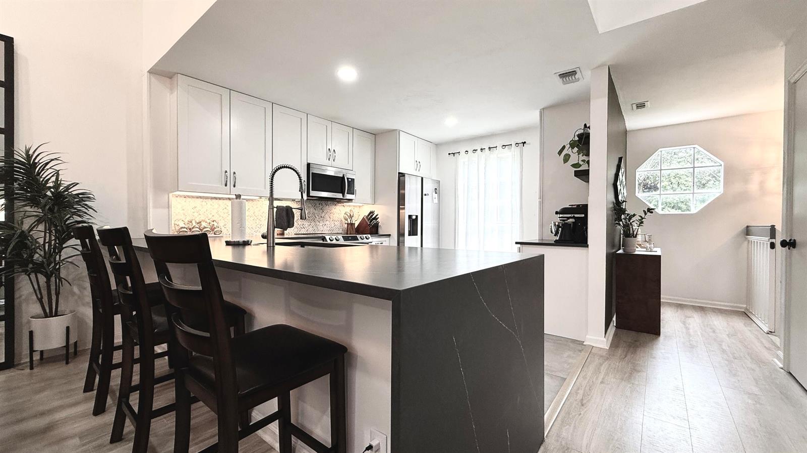 A modern kitchen features white cabinetry, a dark waterfall island, and light wood-look flooring — 5016 Heatherhill Lane # 10, Boca Raton FL 33486, BOCA RATON, FL