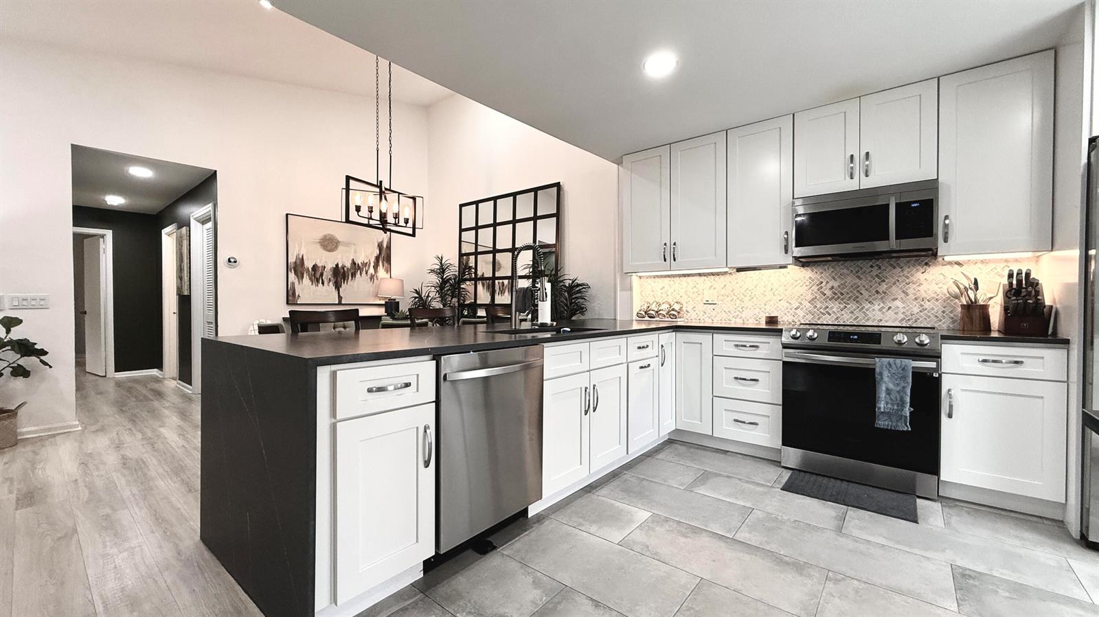 A modern kitchen features white cabinets, dark countertops, stainless steel appliances, and a tiled backsplash — 5016 Heatherhill Lane # 10, Boca Raton FL 33486, BOCA RATON, FL