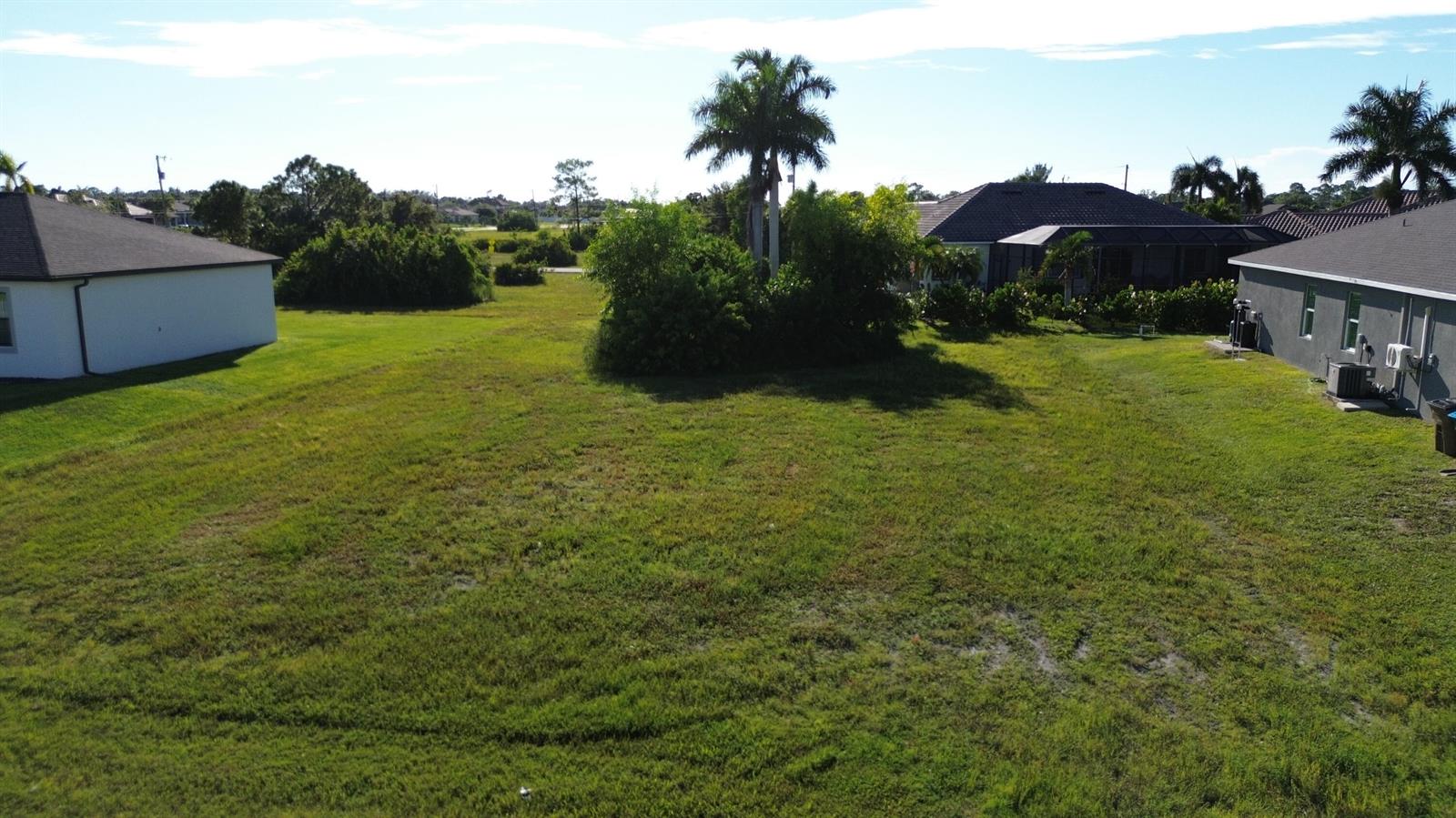 An aerial view shows a grassy vacant residential lot situated between two houses — 2012 NW 24th Place, Cape Coral FL 33993, CAPE CORAL, FL