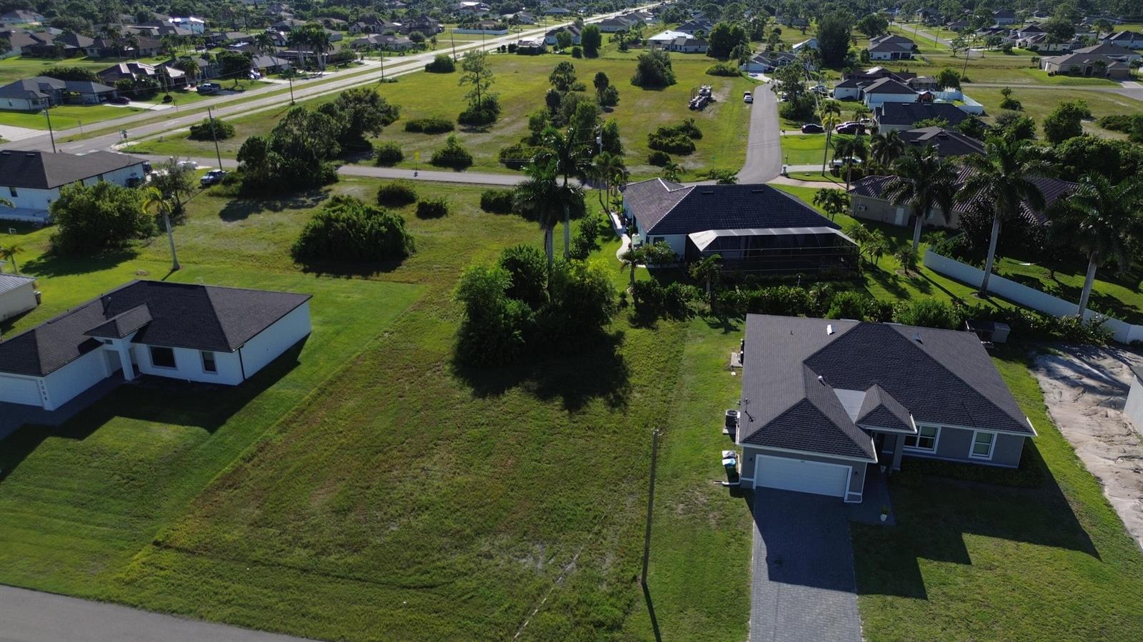 An aerial view shows two suburban houses separated by a large, undeveloped grassy lot — 2012 NW 24th Place, Cape Coral FL 33993, CAPE CORAL, FL