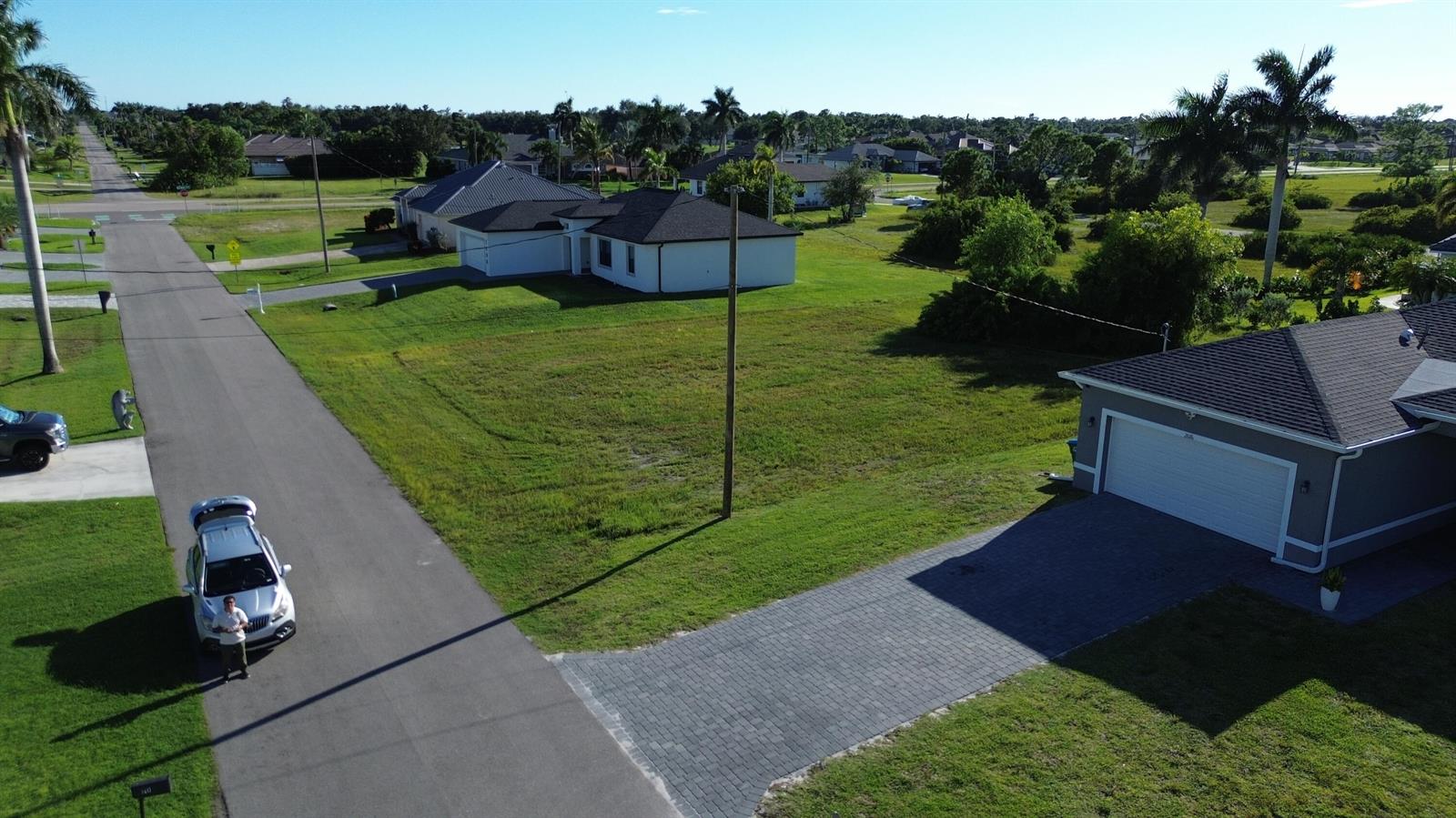 An aerial view shows a residential street with a vacant lot between two suburban houses — 2012 NW 24th Place, Cape Coral FL 33993, CAPE CORAL, FL