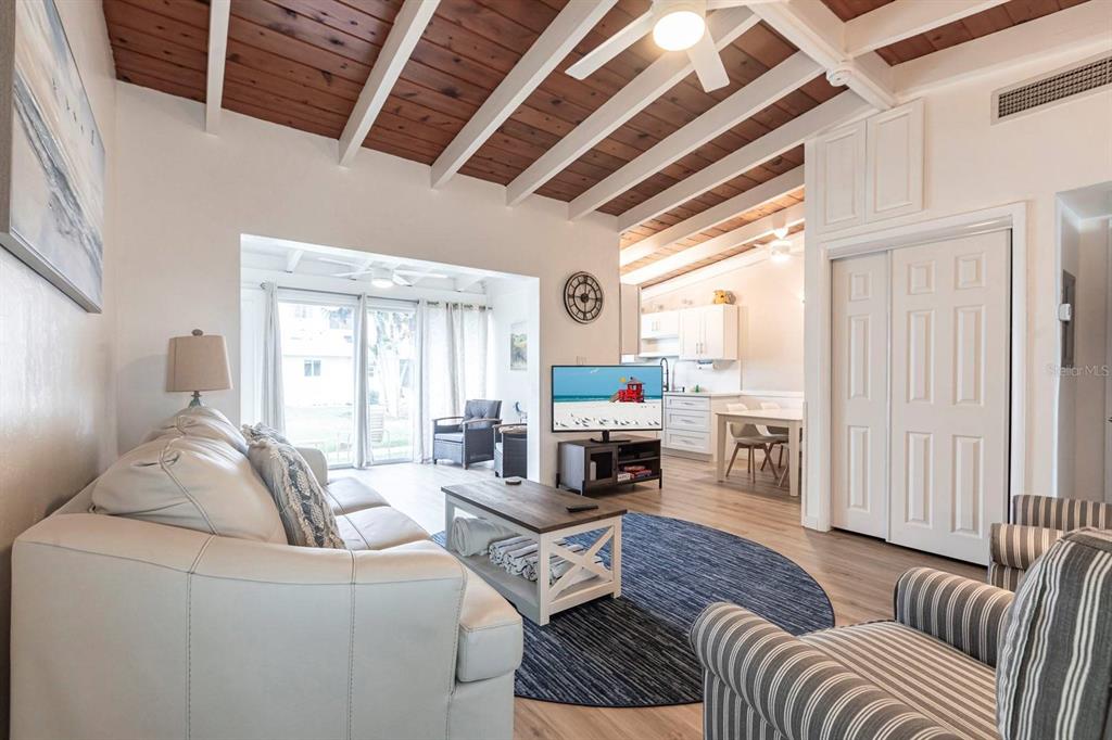 A living room features a vaulted wood-beam ceiling, white furniture, and a blue area rug — 6006 MIDNIGHT PASS ROAD UNIT 54, SARASOTA, FL