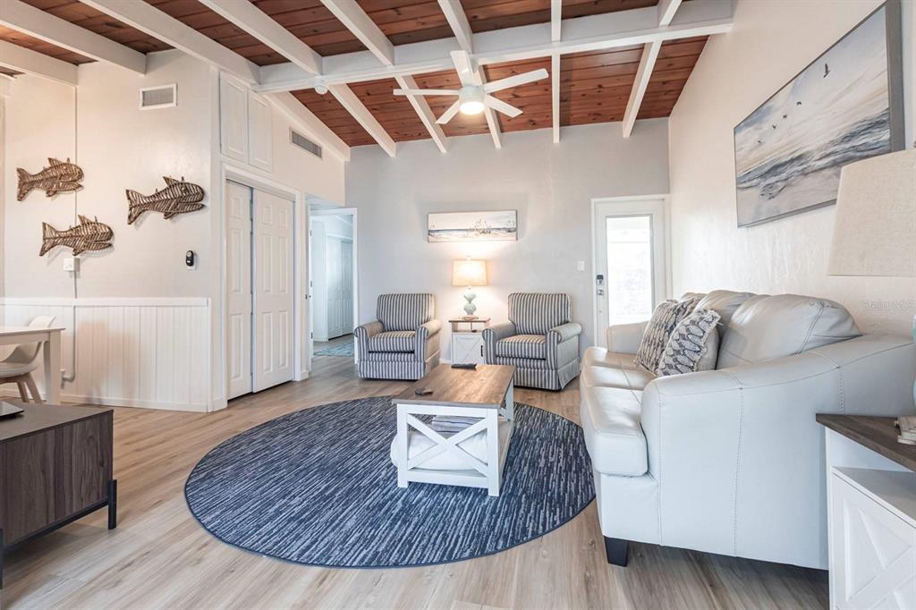 A living room features a vaulted wood-beam ceiling, white walls, and a blue circular rug — 6006 MIDNIGHT PASS ROAD UNIT 54, SARASOTA, FL