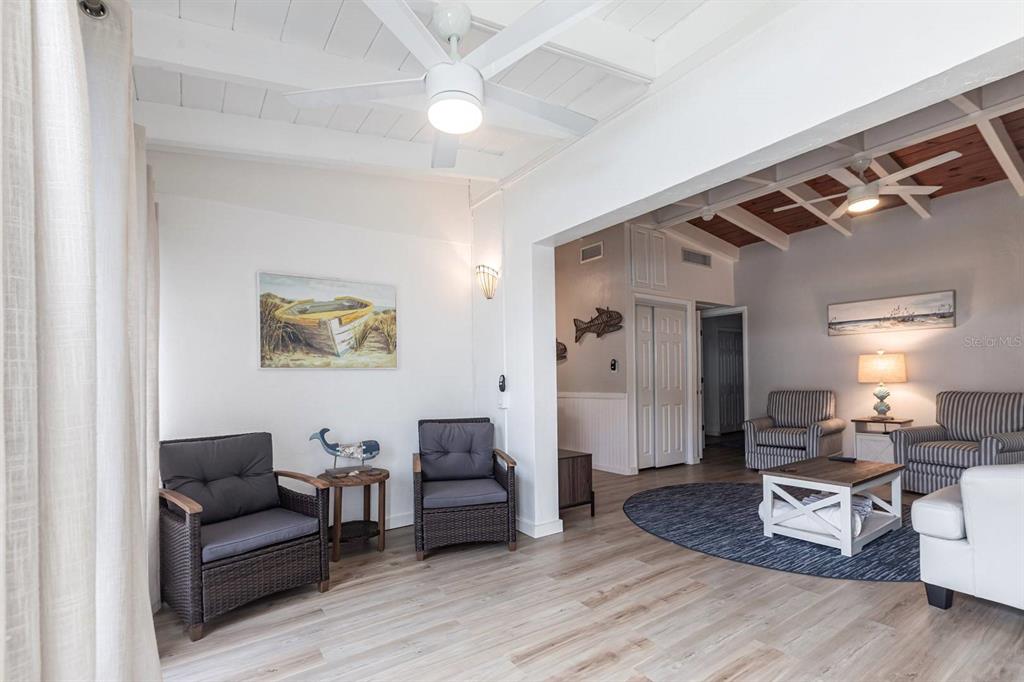 A living room features light wood flooring, white vaulted ceilings, and coastal-themed decor — 6006 MIDNIGHT PASS ROAD UNIT 54, SARASOTA, FL