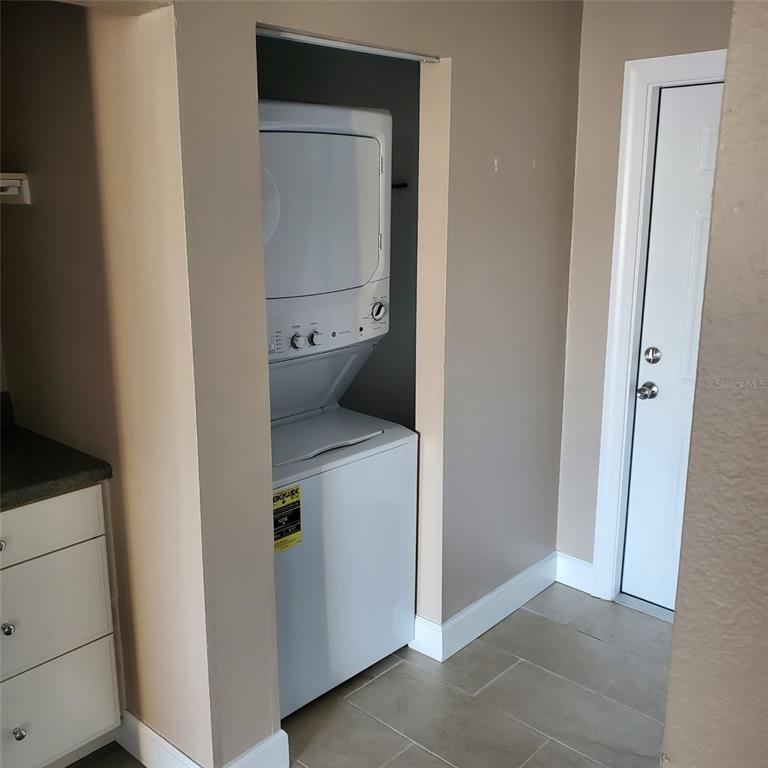 A laundry closet contains a stacked white washer and dryer unit next to a white door — 2504 WOODGATE BOULEVARD UNIT 205, ORLANDO, FL