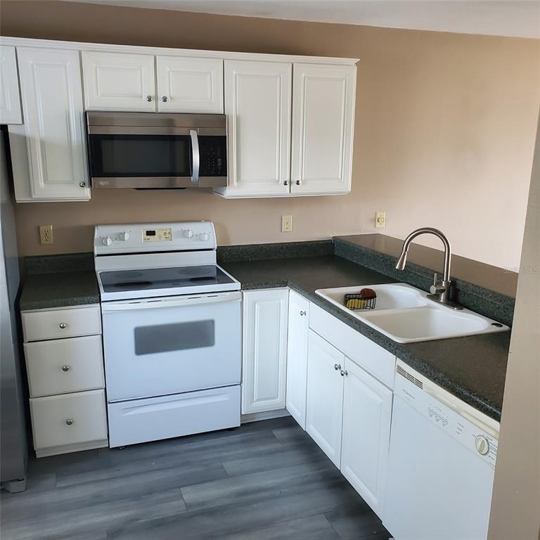 A kitchen features white cabinets, a stainless steel microwave, a white stove, and dark countertops — 2504 WOODGATE BOULEVARD UNIT 205, ORLANDO, FL