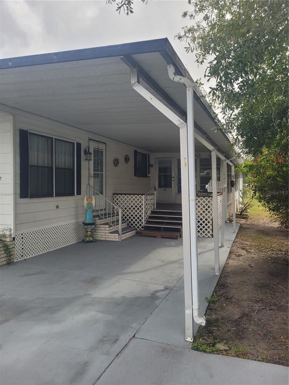 A mobile home exterior features a covered concrete carport, lattice skirting, and two entry staircases — 3027 GALAXY LANE, LAKELAND, FL