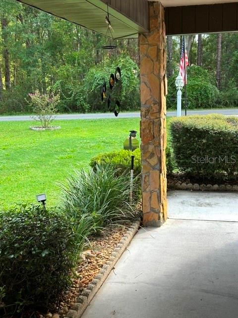A stone-clad porch pillar stands beside a concrete walkway overlooking a grassy yard and woods — 10335 N ABBY DRIVE, CITRUS SPRINGS, FL