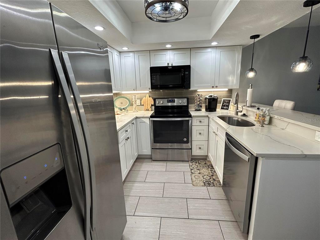 A kitchen features white cabinets, stainless steel appliances, quartz countertops, and light-colored tile flooring — 6301 MANATEE AVENUE W, BRADENTON, FL
