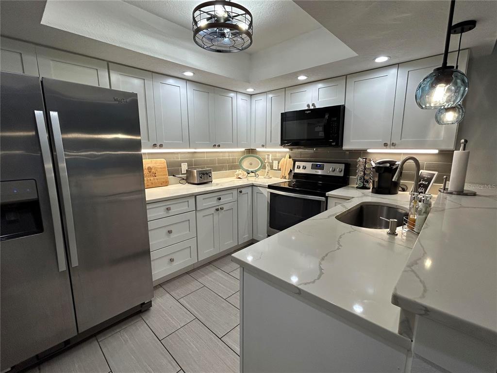 A modern kitchen features white cabinetry, quartz countertops, stainless steel appliances, and tile flooring — 6301 MANATEE AVENUE W, BRADENTON, FL