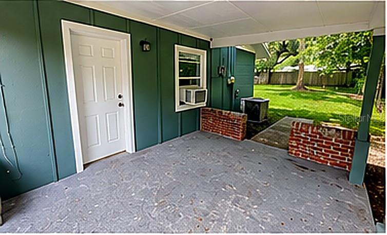 A covered patio with green siding, a white door, a window unit, and brick accents — 1415 NE 53RD STREET, OCALA, FL