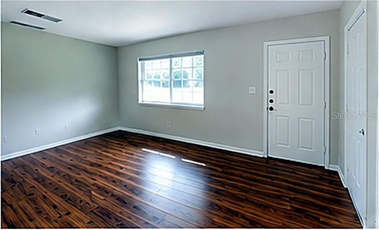 An empty room features dark wood-look flooring, light gray walls, a window, and two doors — 1415 NE 53RD STREET, OCALA, FL