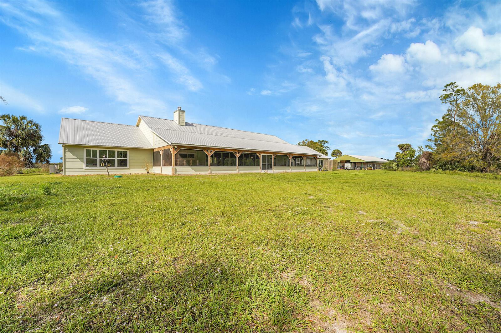 A light-colored house with a metal roof and a screened-in porch sits on a lawn — 3901 Wild Turkey Trail Trail, Okeechobee FL 34974, OKEECHOBEE, FL