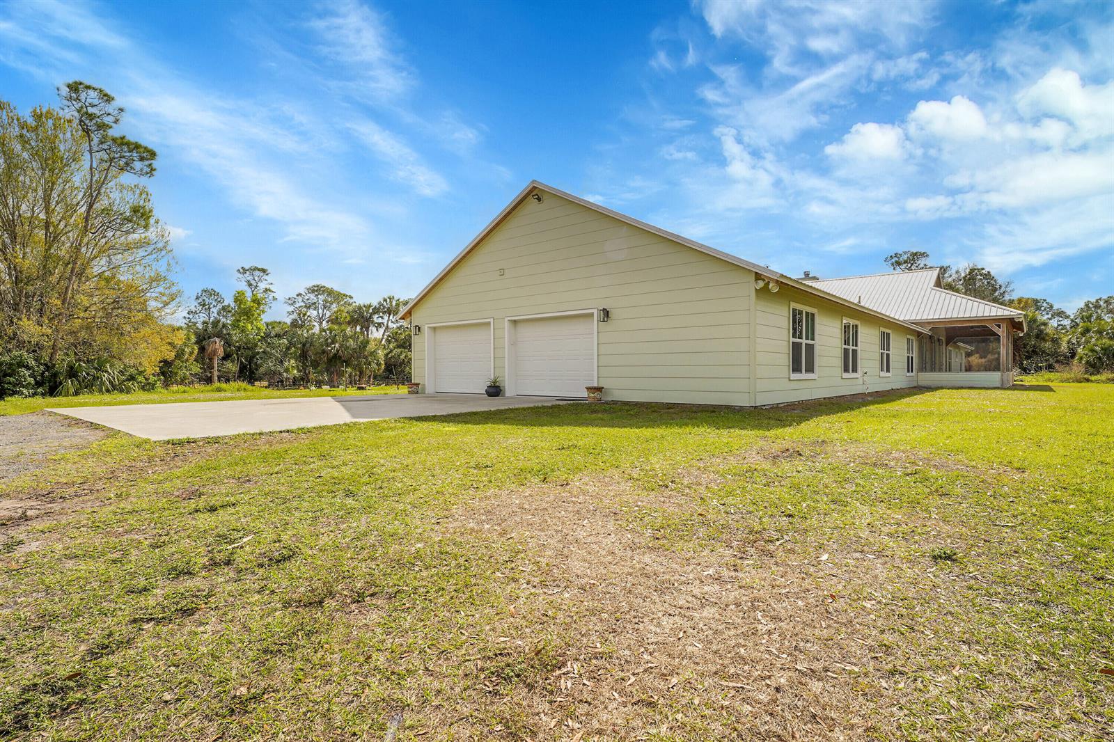 The exterior of a light green house features a two-car garage and a screened porch — 3901 Wild Turkey Trail Trail, Okeechobee FL 34974, OKEECHOBEE, FL