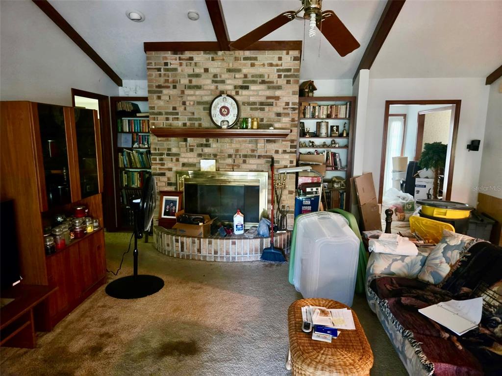A living room features a brick fireplace, built-in bookshelves, a ceiling fan, and carpeted flooring — 741 BRECHNER TERRACE, DELTONA, FL