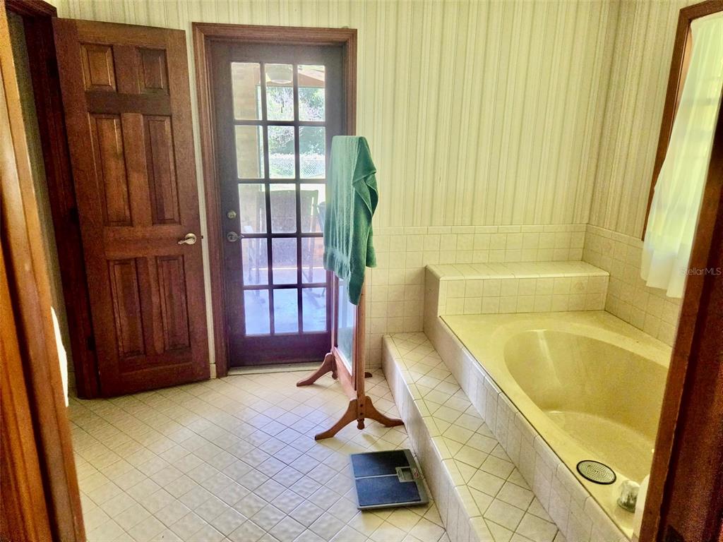A bathroom features a built-in soaking tub, tile flooring, wallpaper, and a glass-paned exterior door — 741 BRECHNER TERRACE, DELTONA, FL