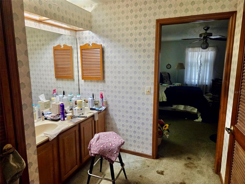 A bathroom with a vanity, patterned wallpaper, and carpeted flooring leads into a bedroom — 741 BRECHNER TERRACE, DELTONA, FL