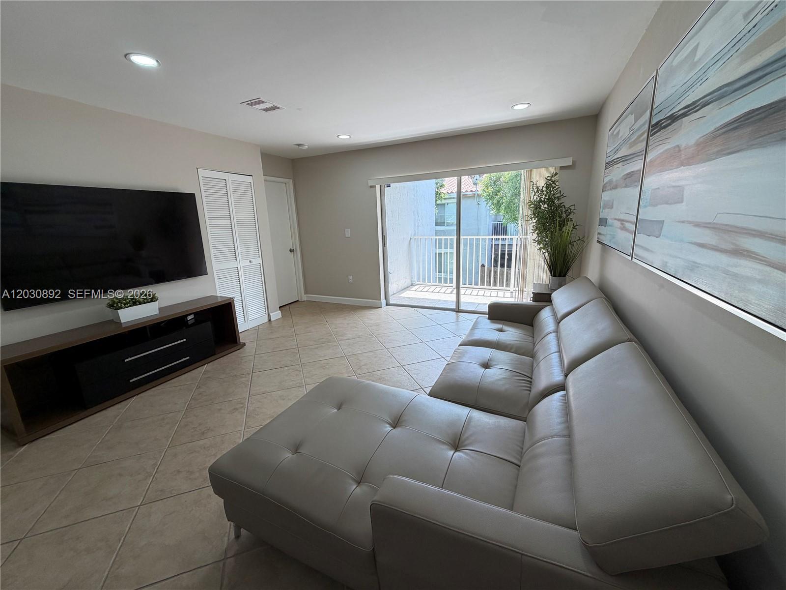 A living room features a sectional sofa, a wall-mounted television, and a sliding glass door — 4712 NW 114th Ave # 202, Doral FL 33178, DORAL, FL