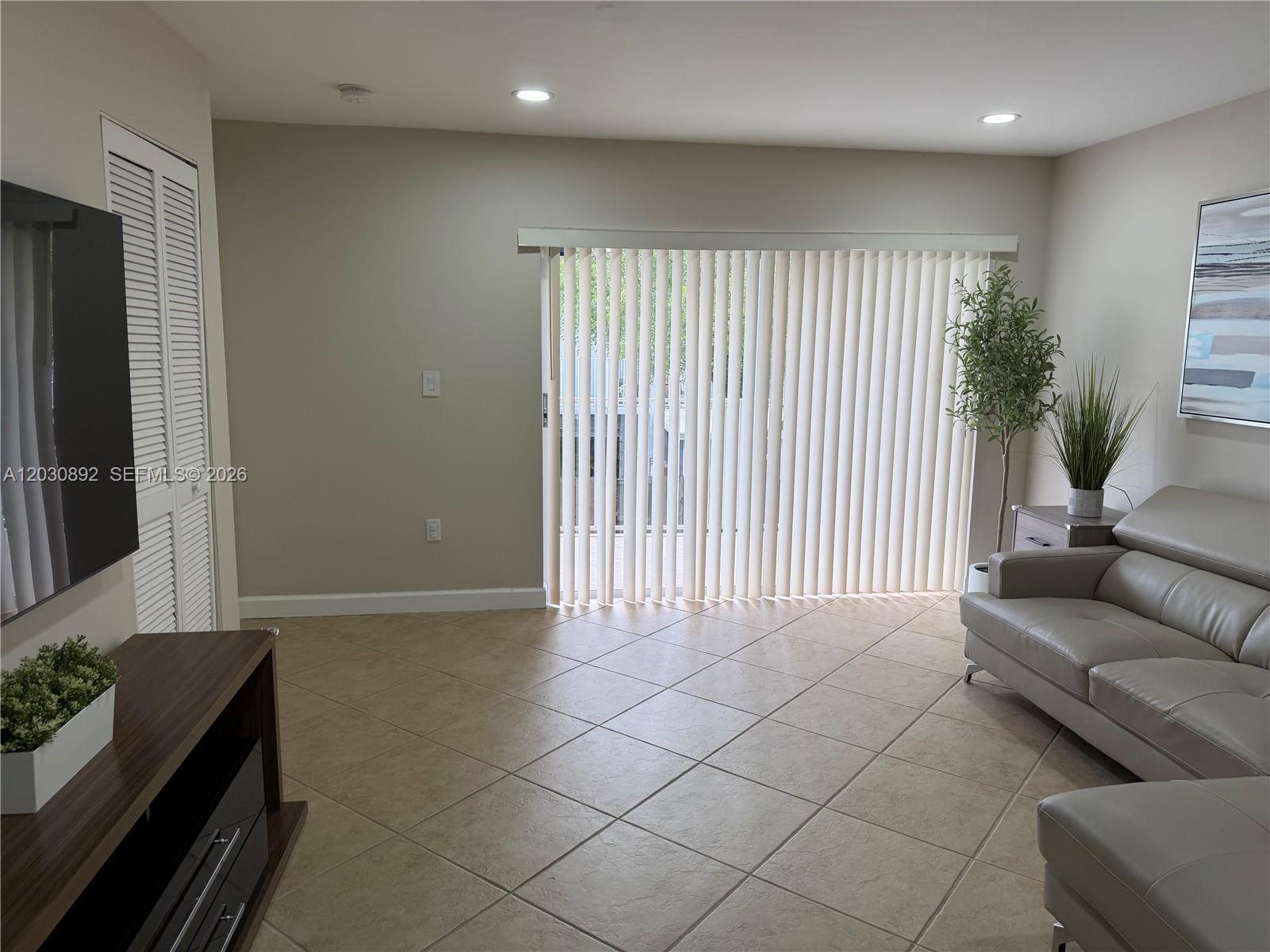 A living room features tile flooring, vertical blinds over a sliding door, and a sofa — 4712 NW 114th Ave # 202, Doral FL 33178, DORAL, FL