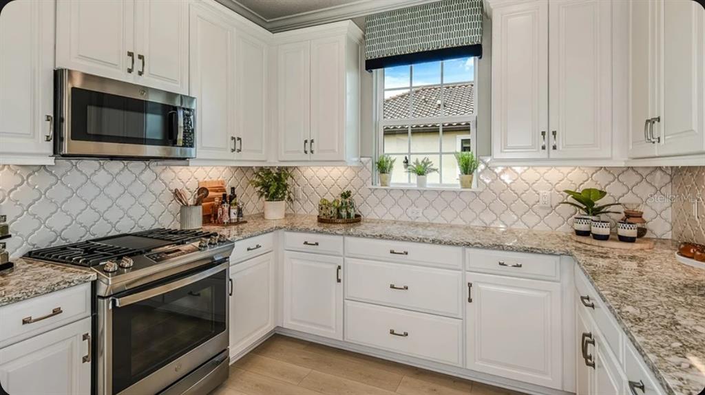 A kitchen with white cabinets, stainless steel appliances, granite countertops, and a patterned tile backsplash — 14517 DERNA TERRACE, BRADENTON, FL