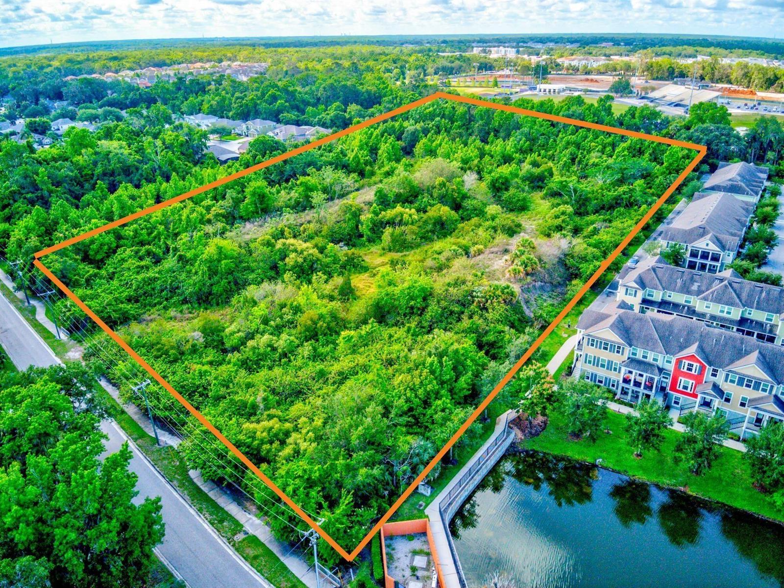 An aerial view shows a rectangular, tree-covered vacant lot bordered by a road and townhomes — 1205 Orange Avenue, FL 32708, FL