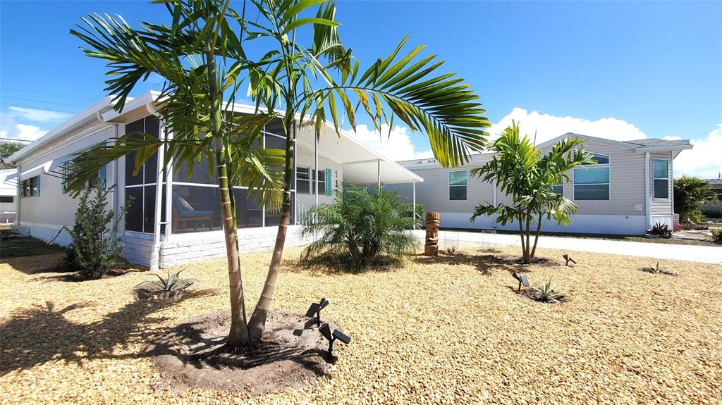 The exterior of a manufactured home features a screened-in porch, palm trees, and gravel landscaping — 712 CAREFREE, VENICE, FL