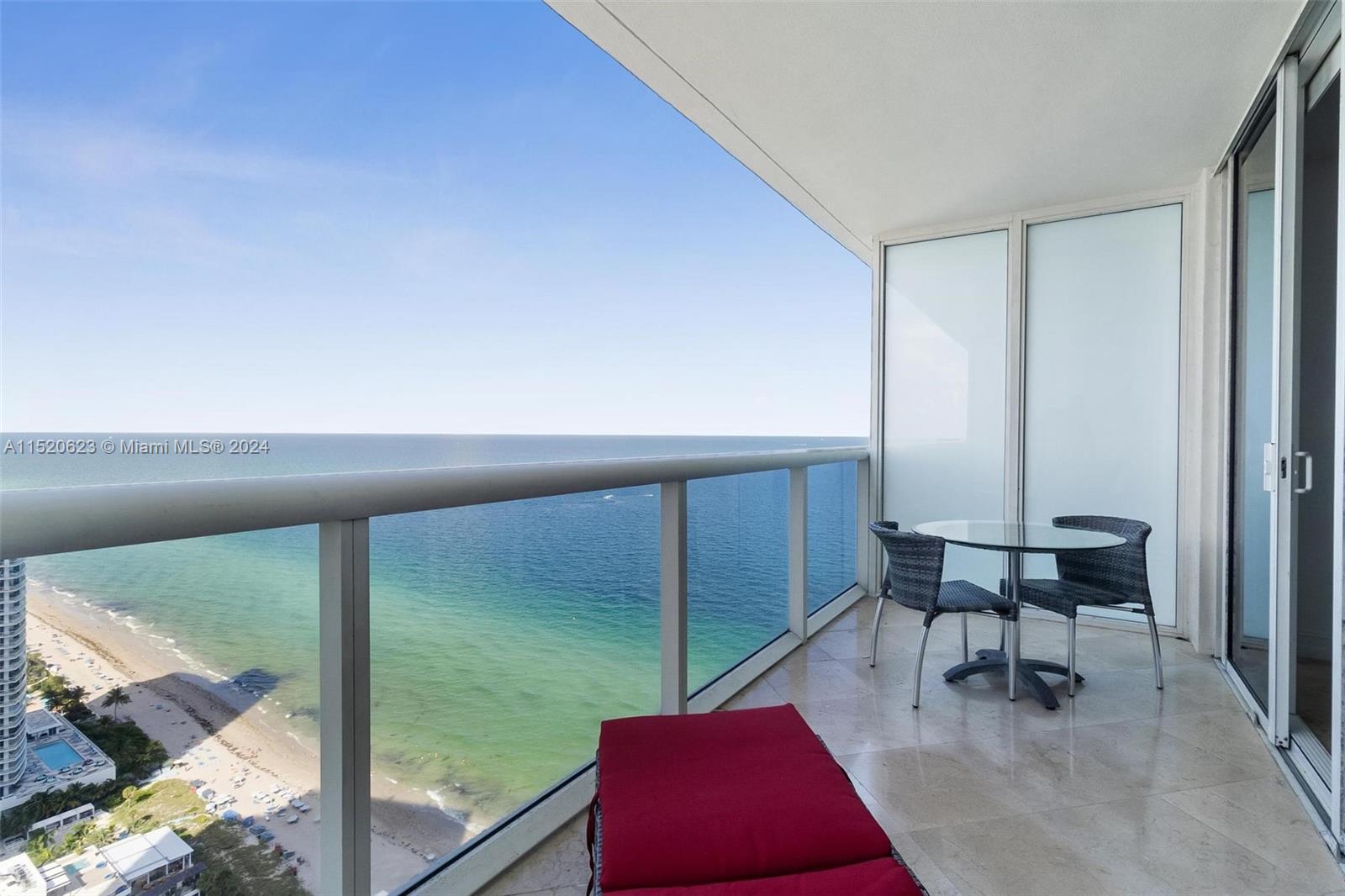 A balcony with a glass railing overlooks the ocean and beach, featuring a small table — 1830 S Ocean Dr # 3809, Hallandale Beach FL 33009, HALLANDALE BEACH, FL