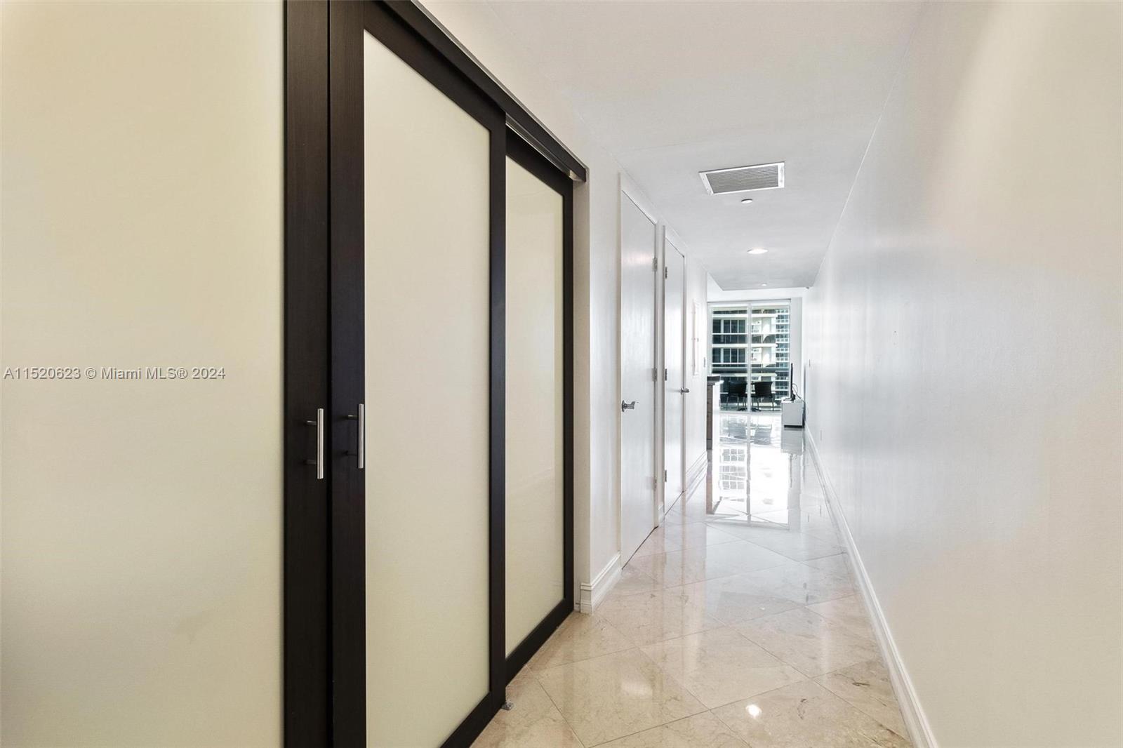 A hallway with light-colored tile flooring leads toward a balcony with a glass sliding door — 1830 S Ocean Dr # 3809, Hallandale Beach FL 33009, HALLANDALE BEACH, FL