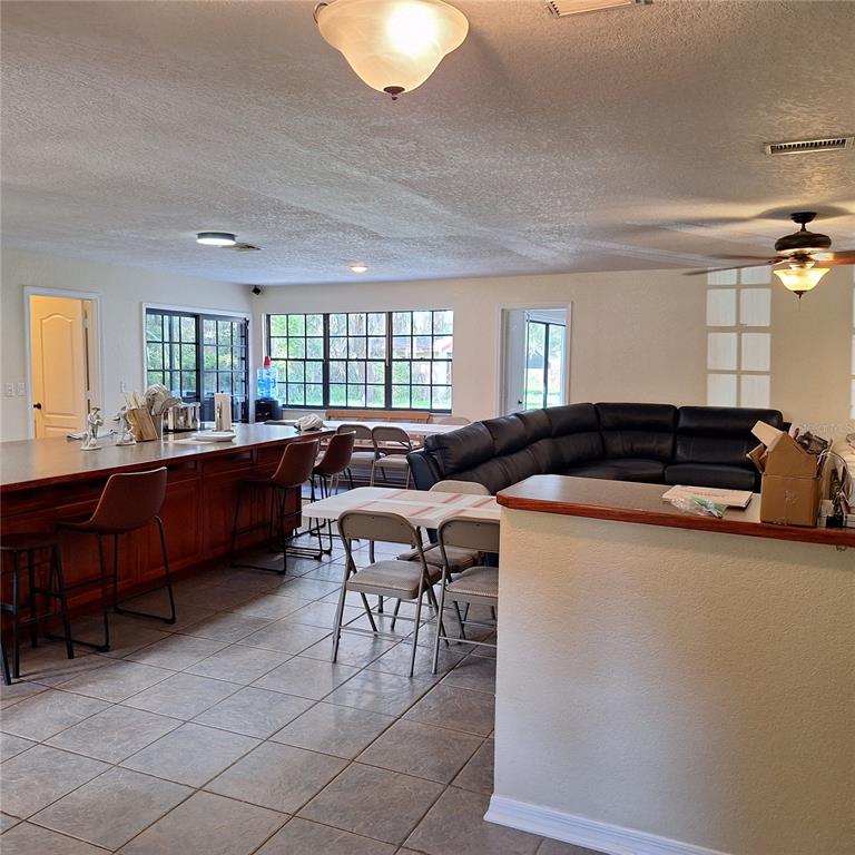 An open-concept kitchen and living area features a large island, tile flooring, and dark furniture — 10012 LAKE LOUISA ROAD, CLERMONT, FL