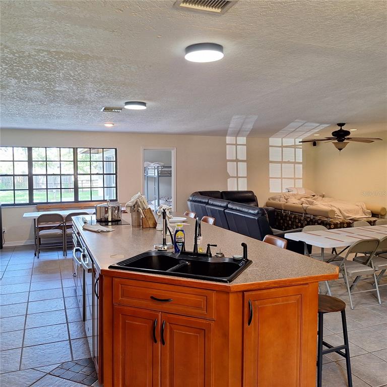 A kitchen island with a black sink sits in an open-concept room with dining tables — 10012 LAKE LOUISA ROAD, CLERMONT, FL