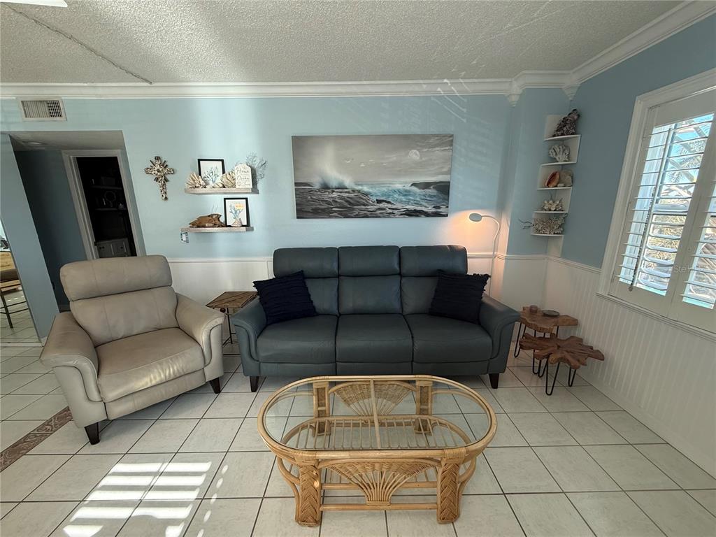 A living room features a blue sofa, a beige recliner, and a glass-topped rattan coffee table — 18650 GULF BLVD UNIT 316, INDIAN SHORES, FL