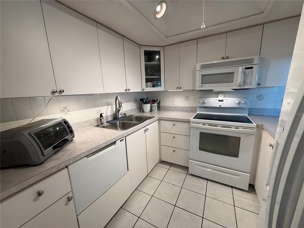 A kitchen features white cabinets, white appliances, a double sink, and light-colored tile flooring — 18650 GULF BLVD UNIT 316, INDIAN SHORES, FL