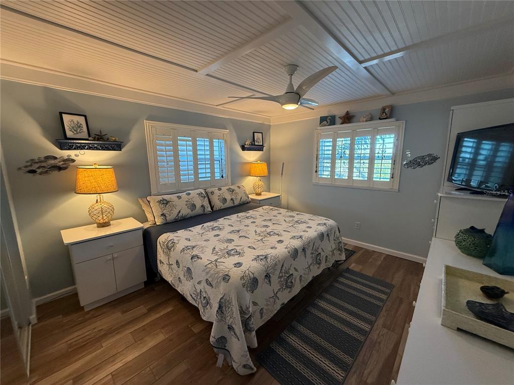 A bedroom features a queen bed, coastal decor, white shutters, and wood-look flooring — 18650 GULF BLVD UNIT 316, INDIAN SHORES, FL