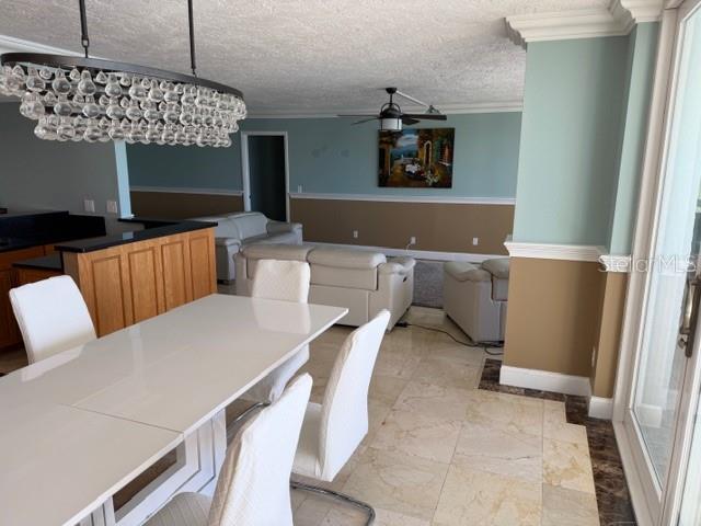 A dining area with a glass chandelier overlooks a living room with light-colored furniture — 17900 GULF BOULEVARD UNIT 18C, ST PETERSBURG, FL