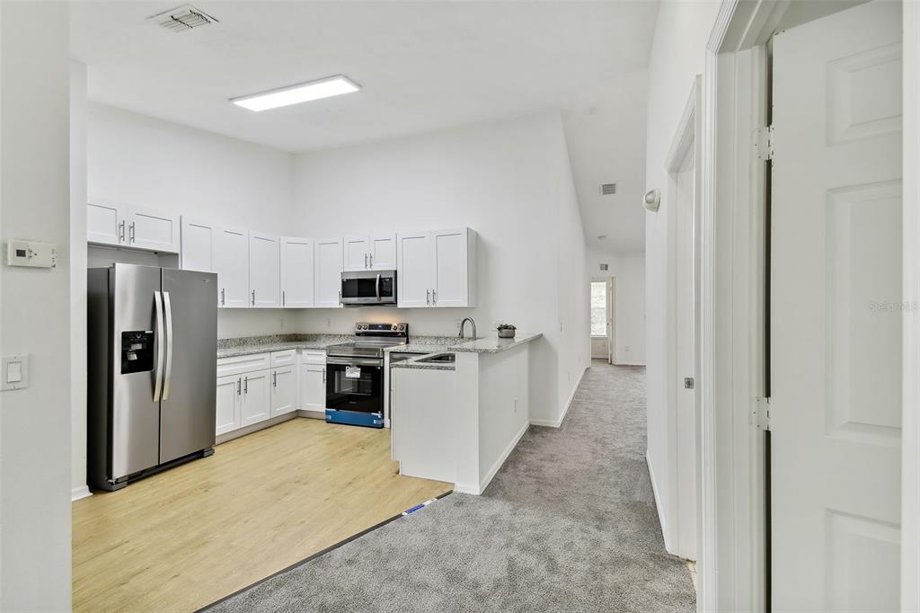 A kitchen with white cabinets, stainless steel appliances, and light wood flooring opens to carpet — 8827 GRAND PALMS CIRCLE UNIT B, KISSIMMEE, FL