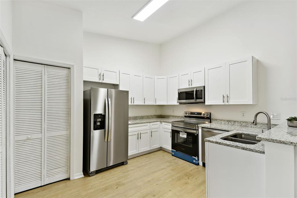 A kitchen features white cabinets, stainless steel appliances, granite countertops, and light wood-look flooring — 8827 GRAND PALMS CIRCLE UNIT B, KISSIMMEE, FL
