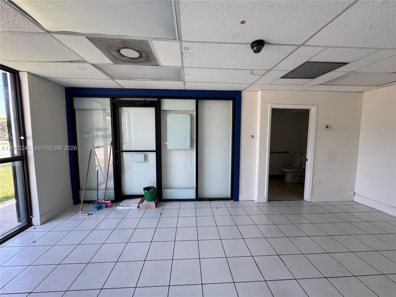 An interior view shows a tiled room with a glass-paneled entrance and a restroom door — 90 NW 79th Ave, Miami FL 33126, MIAMI, FL